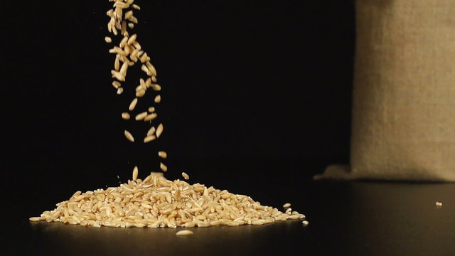 SLOW (240fps): A oats fall in a pile on a table. A cloth bag stands on a background
