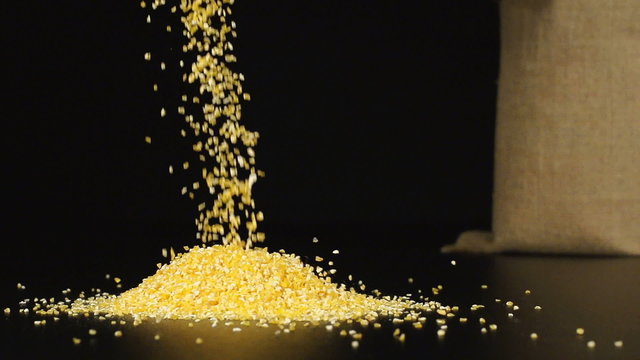 SLOW (240fps): A corn gifts fall in a pile on a table. A cloth bag stands on a background
