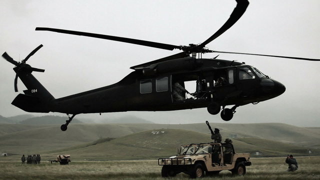 Shot of Black Hawk helicopter attaching and hauling off Humvee from field.