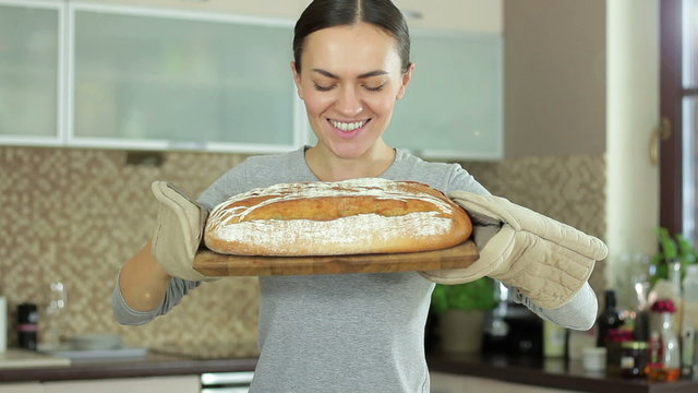 A young smiling woman standing in her kitchen holding freshly baked bread 