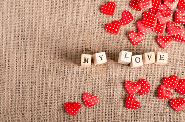 Words "My love " on wooden cubes and many red decorative hearts on sackcloth, canvas background. Vintage style.