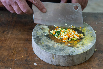 A person prepares vegetables on a wood cutting board.