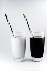 Two glasses with white and black drink and striped straw/Minimalistic black and white composition on a white background