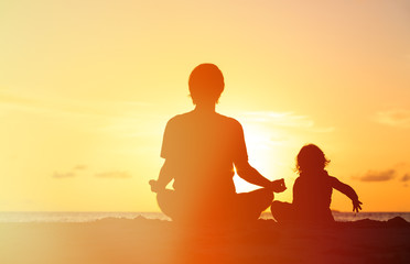 father and little daughter doing yoga at sunset
