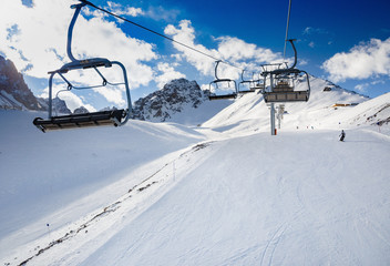 Fototapeta na wymiar Winter mountains panorama with ski slopes and ski lifts. Skiers going down the slope under ski lift.