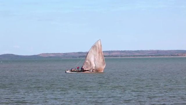 Static shot of sailboat floating by as the wind blows its sail.