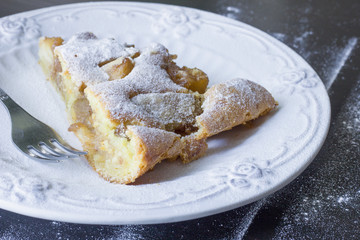 delicious piece of hot apple pie sprinkled with powdered sugar on a white plate elegant.  Black wood background.