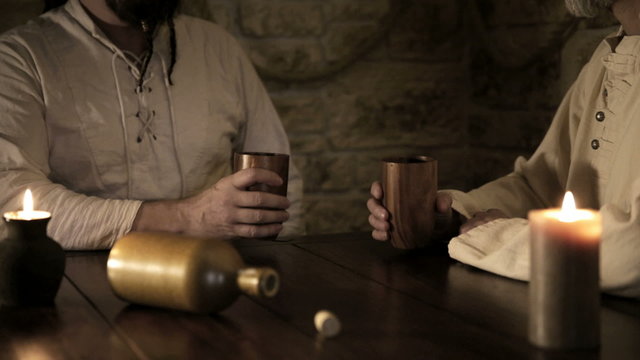 two medieval looking men are clicking their cups, than drinking, vintage filtered