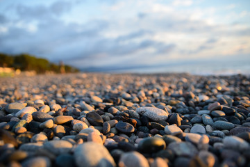 sunset on the pebbly beach, in the background the sky with clouds, foreground round stones