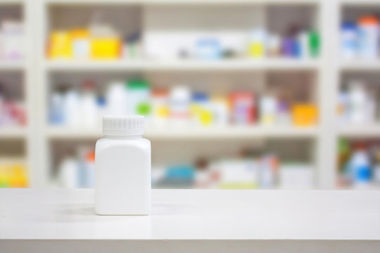 Blank white medicine bottle on counter with blur shelves of drug