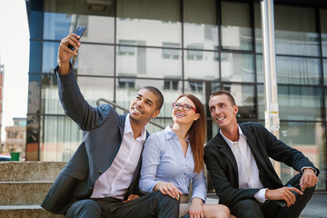 Group of business people sitting at stairs in front of their office and making selife.