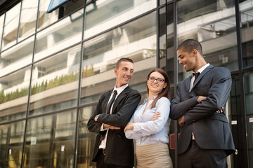 Group of business people standing in front of a glassy building, looking each other and smiling.