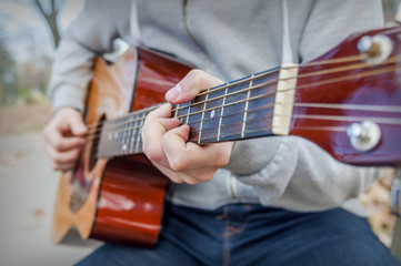 Young man playing acoustic guitar close up outdoors in autumn park
