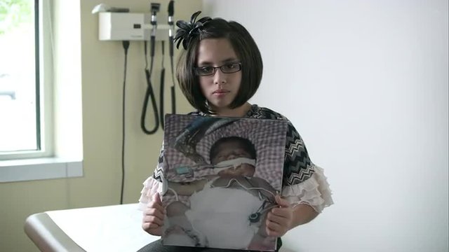 Slow motion of young girl holding up photo of herself when she was a baby in the hospital.