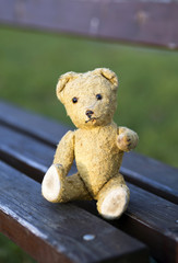 Toy bear sitting on a bench and giving his paw