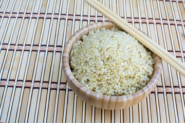 Cooked quinoa in bamboo bowl and chopsticks on bamboo platemat