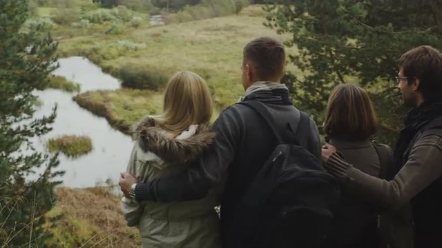 Two couples are looking at a forest landscape with a lake from a mountain. Shot on RED Cinema Camera.