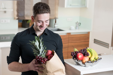 Junger Mann betrachtet lächelnd seinen Obsteinkauf