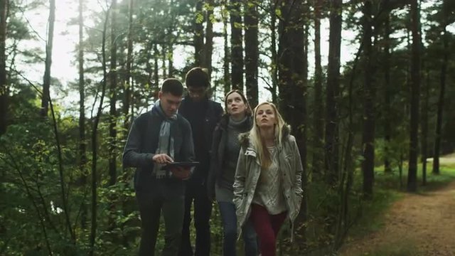 Group of friends are checking tablet in a forest and continuing to move forwards. Shot on RED Cinema Camera.