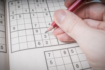 Hand holds pen and is playing sudoku puzzle game.