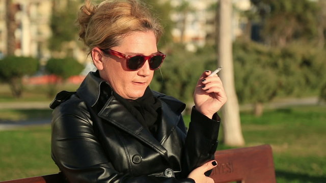 Sad woman sitting on a park bench and smoking cigarette