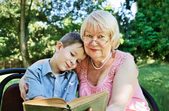 smiling boy and his grandmother reading a book in the park