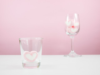 The lovely pink heart marshmallows in shot glass and wine glass on white table.
