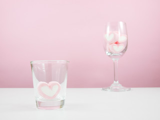 The lovely pink heart marshmallows in shot glass and wine glass on white table.
