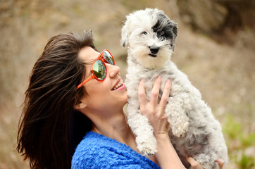 smiling young woman hugging with her small white poodle dog outdoor
