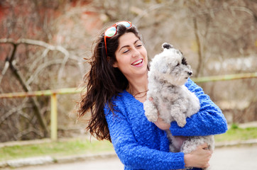 smiling young woman hugging with her small white poodle dog outdoor