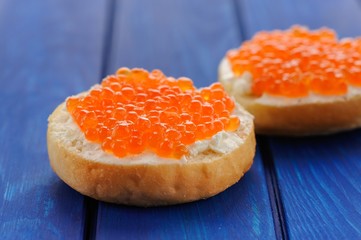 Delicious red caviar on buns with cream cheese on deep blue tabl