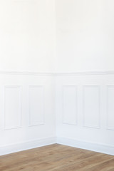 Empty white room corner with parquet floor and wood trimmed wall