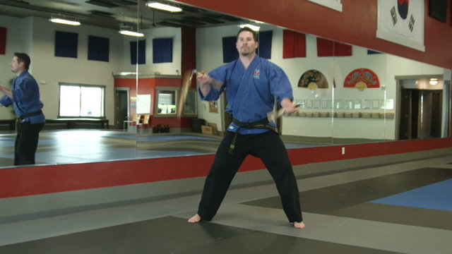 Man in a karate studio practicing nunchuch weapon moves