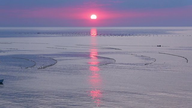 Beautiful sea sunrise view with sun reflection on water and buoys of the dragnets . People on the motorboat are not recognizable.       
