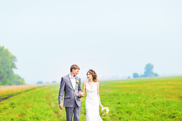 Fototapeta na wymiar happy beautiful bride and groom walking on field