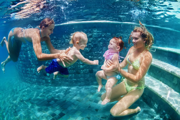 Happy family - 2 mothers with baby daughter and son and dive with fun in beach pool. Active parents lifestyle, people water sport activity and underwater swimming lessons on summer vacation with child