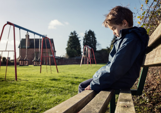 Lonely child with depression sitting on play park playground bench