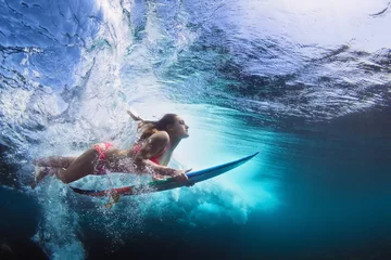 Foto op Aluminium Young girl in bikini - surfer with surf board dive underwater with fun under big ocean wave. Family lifestyle, people water sport lessons and beach swimming activity on summer vacation with child © Tropical studio