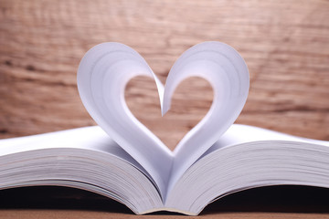 Open book pages into a heart shape.On wood background.