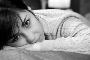 Closeup of young woman lying in bed thinking about lost love unhappy black and white