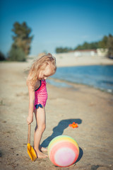 Adorable toddler girl playing with beach toys on white sand beach.