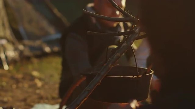 Group of friends are sitting next to a campfire on a sunny day and cook in close-up. Shot on RED Cinema Camera.