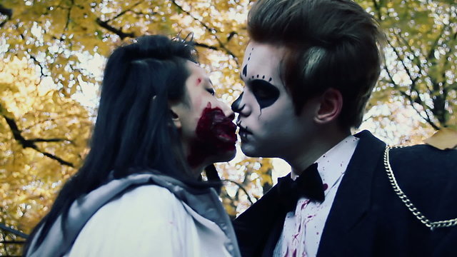 Young couple kissing at Halloween party, man and woman in zombie suits have fun