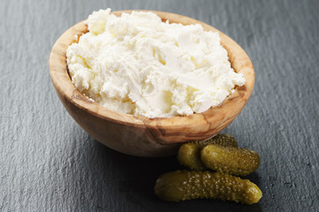 creamy cheese in wooden bowl with small cucumbers