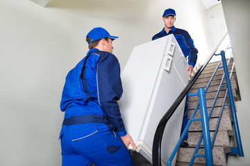 Movers Carrying Refrigerator On Steps At Home