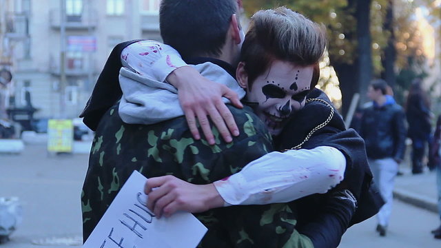 Young men in zombie suits hugging in street, funny flash mob on Halloween