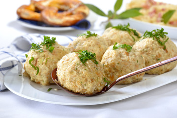 Deftige bayerische Semmelknödel mit Petersilie garniert, eine Breze und Sauerkraut im Hintergrund