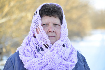 Elderly woman in lilac knitted scarf on her head outdoors