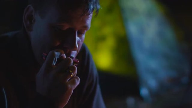 Senior man is playing on a harmonica next to campfire at night while a group of friends are listening. Shot on RED Cinema Camera.