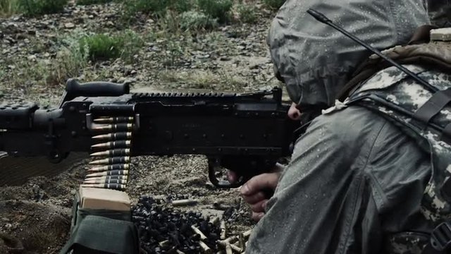 Shot of a soldier firing a belt-fed machine gun from a sitting position.